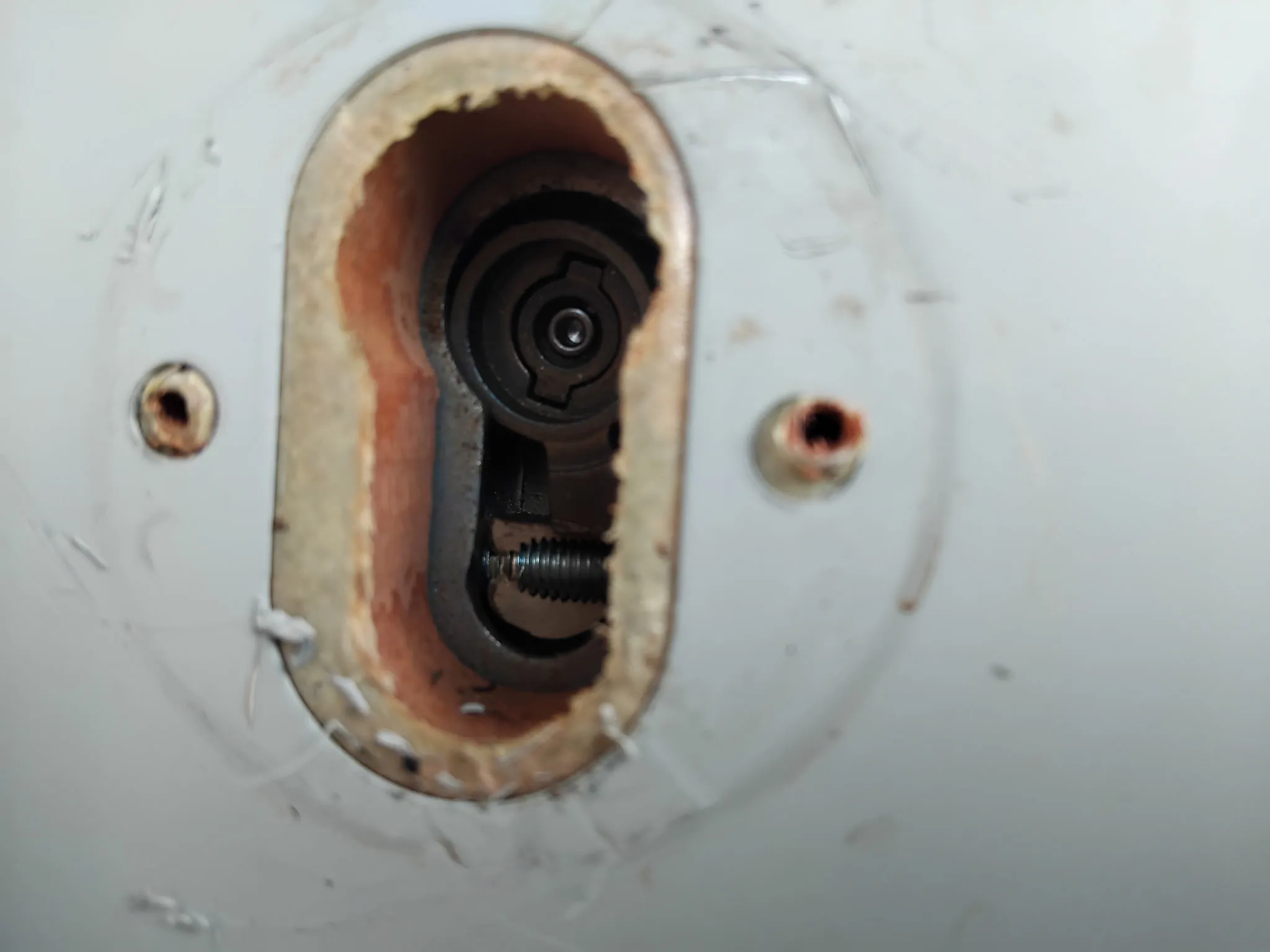 Gros plan sur un cylindre et le mécanisme d'une serrure démontée dans une porte blanche.