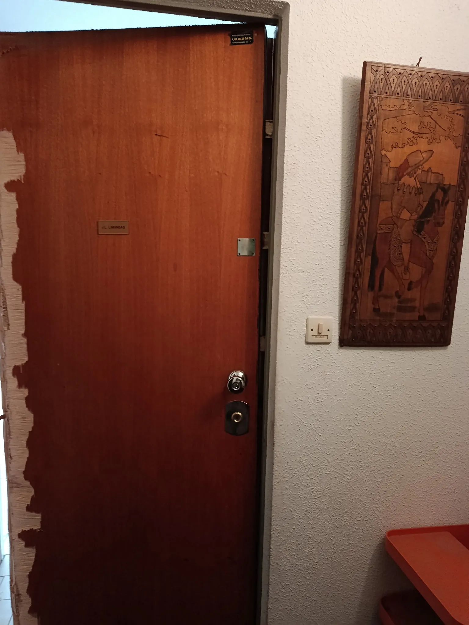 Porte d'entrée en bois entrouverte, avec deux serrures visibles, dans un intérieur aux murs clairs.