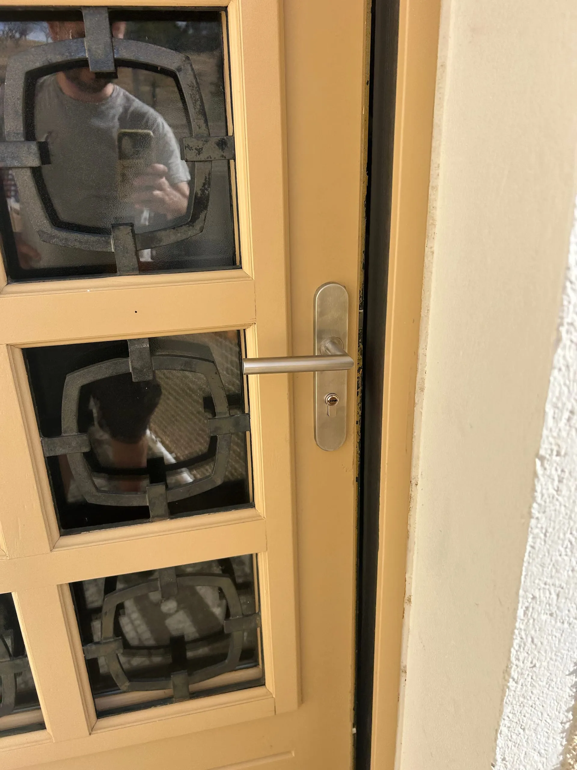 Porte d’entrée vitrée beige équipée d’une poignée double béquille et d’un cylindre européen neufs.