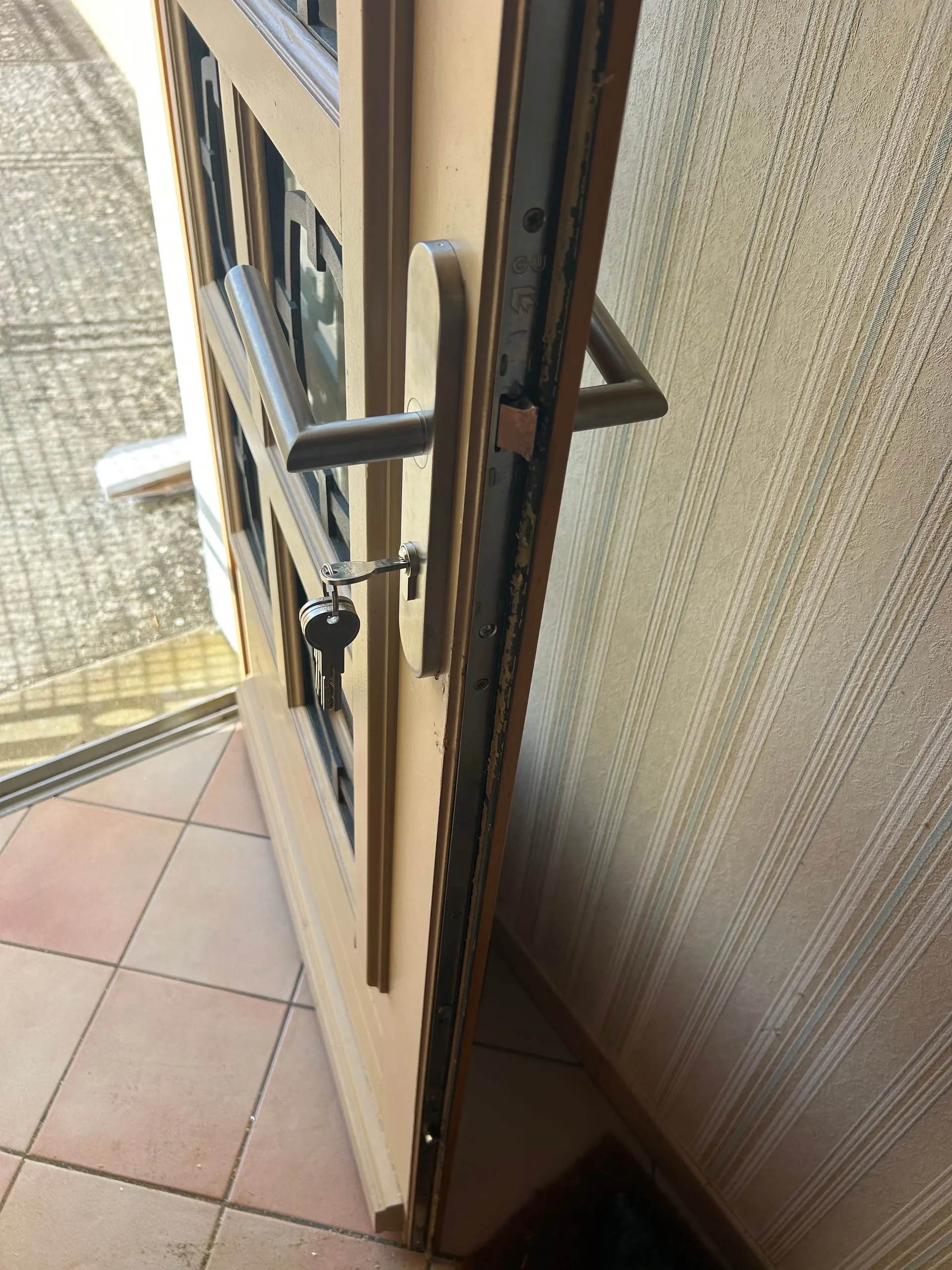 Porte vitrée beige entrouverte avec sa crémone à galets visible sur le chant.