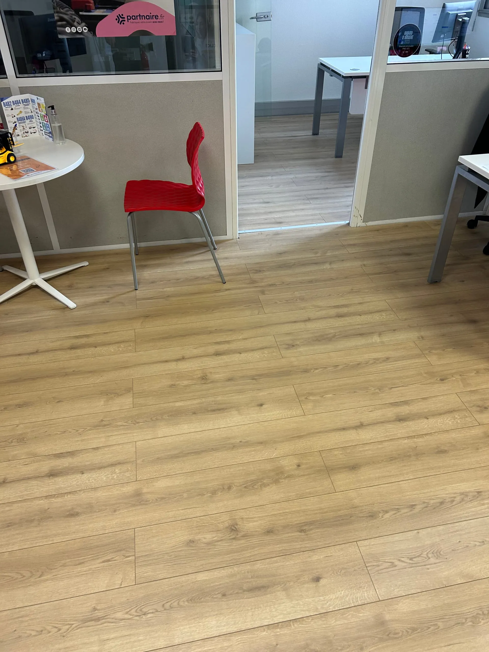 Parquet flottant bois posé dans l’accueil d’une agence d’intérim, avec tables, chaise rouge et porte vitrée.