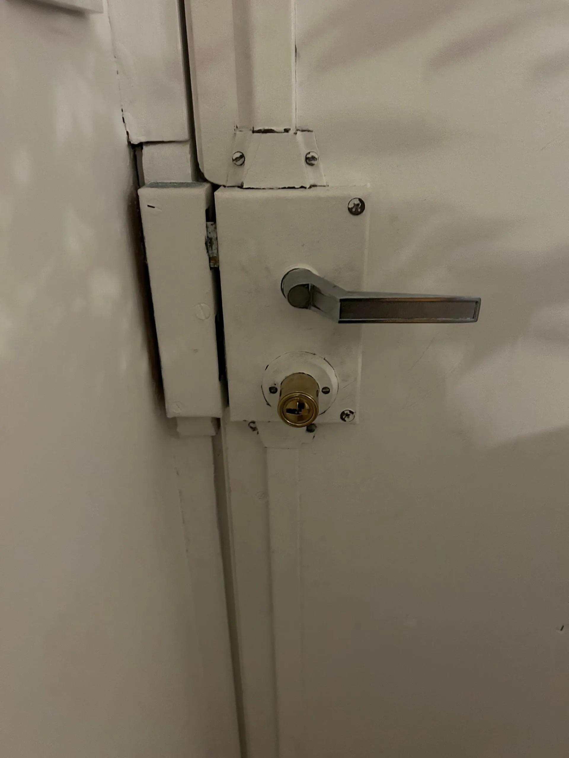 Ancienne serrure Fichet 2D blanche avec poignée et cylindre doré sur le côté intérieur de la porte.