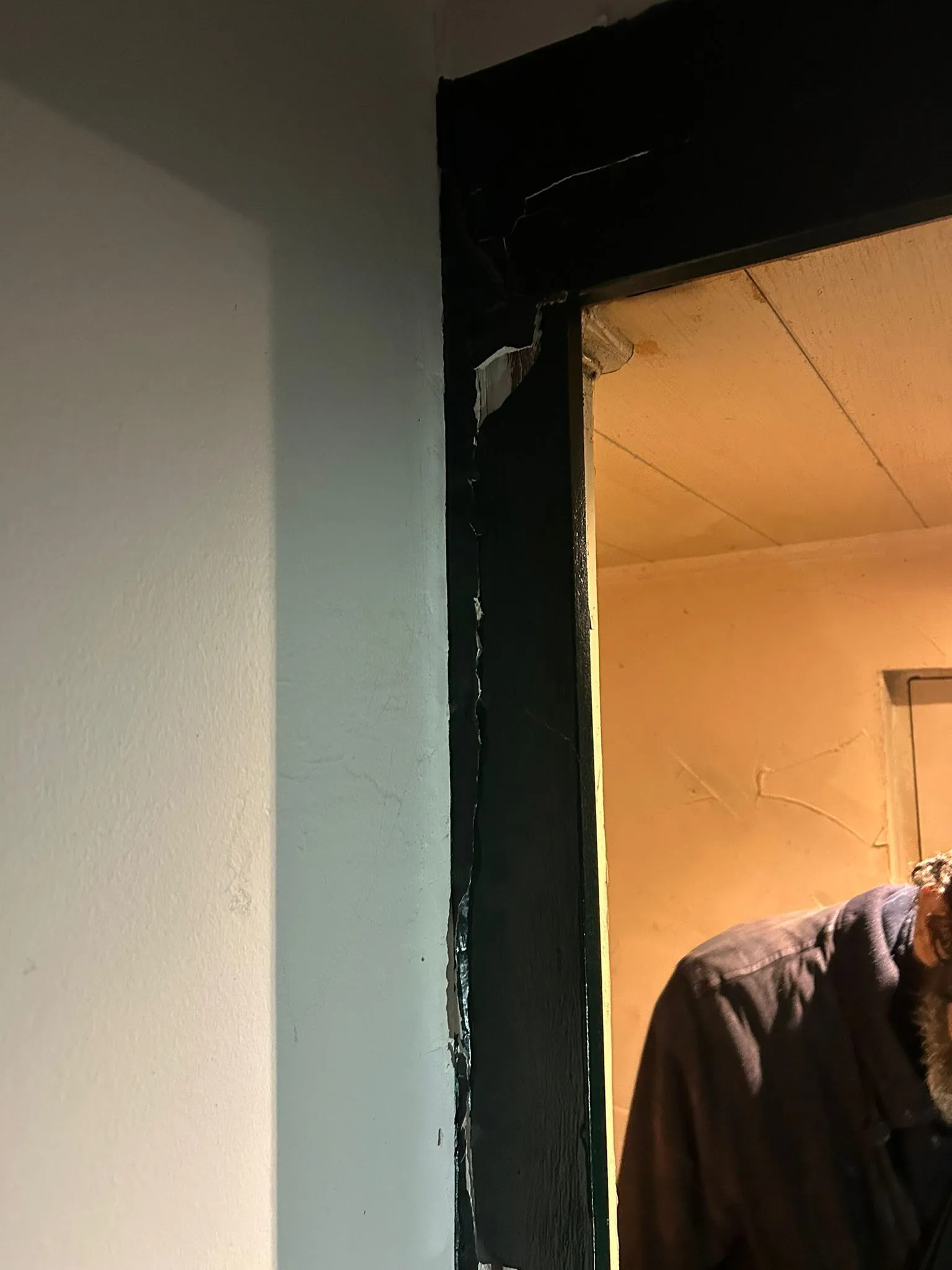 Partie haute d’un cadre de porte vert avec peinture et bois arrachés.