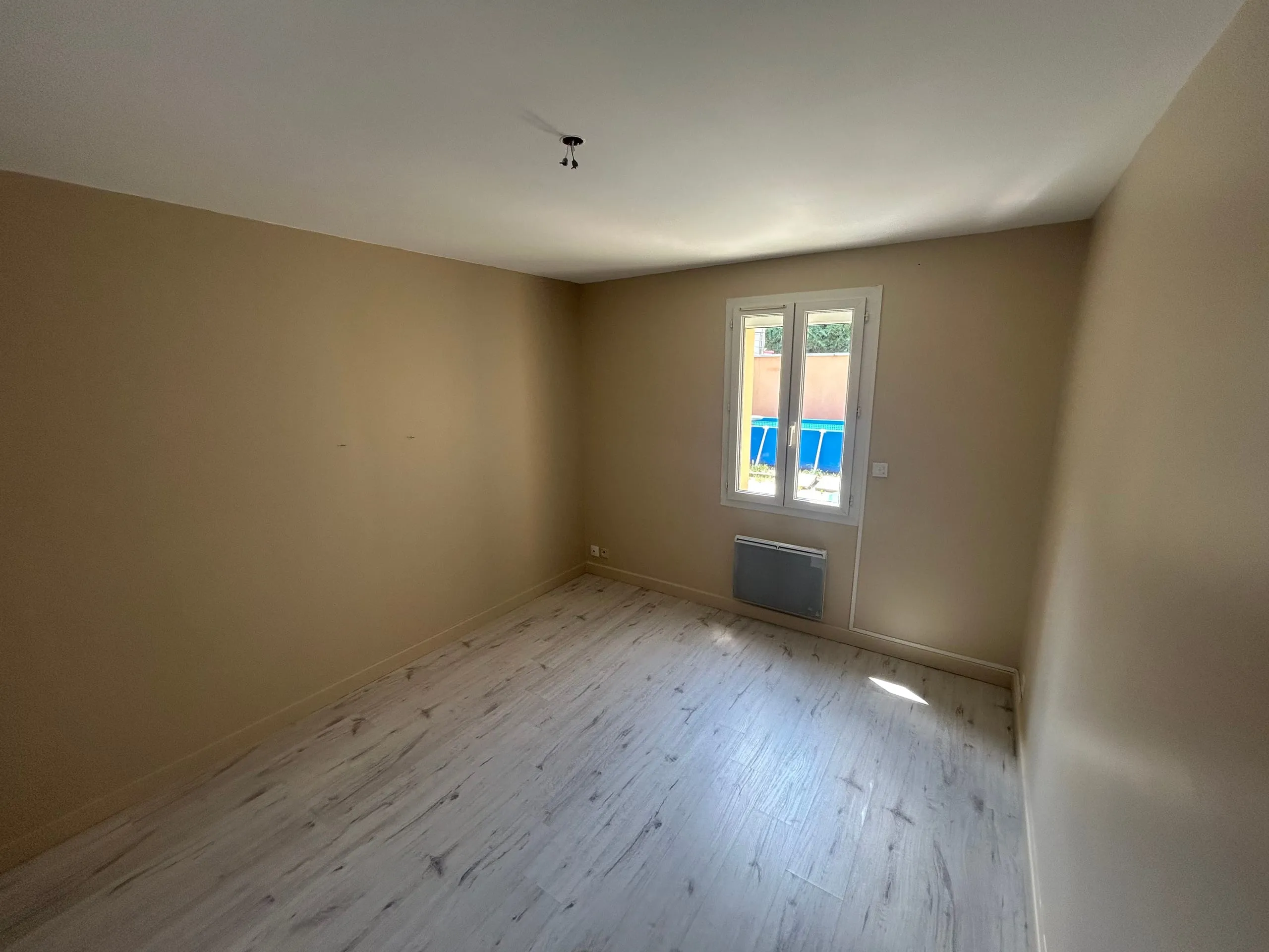 Chambre d’enfant rénovée avec murs beige clair, plafond blanc et fenêtre donnant sur le jardin.
