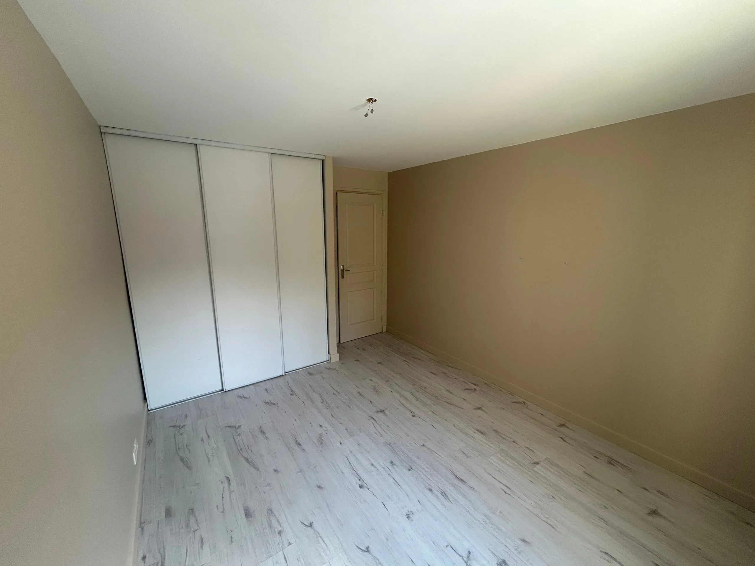 Chambre rénovée avec murs beige clair, plafond blanc et placard coulissant blanc.