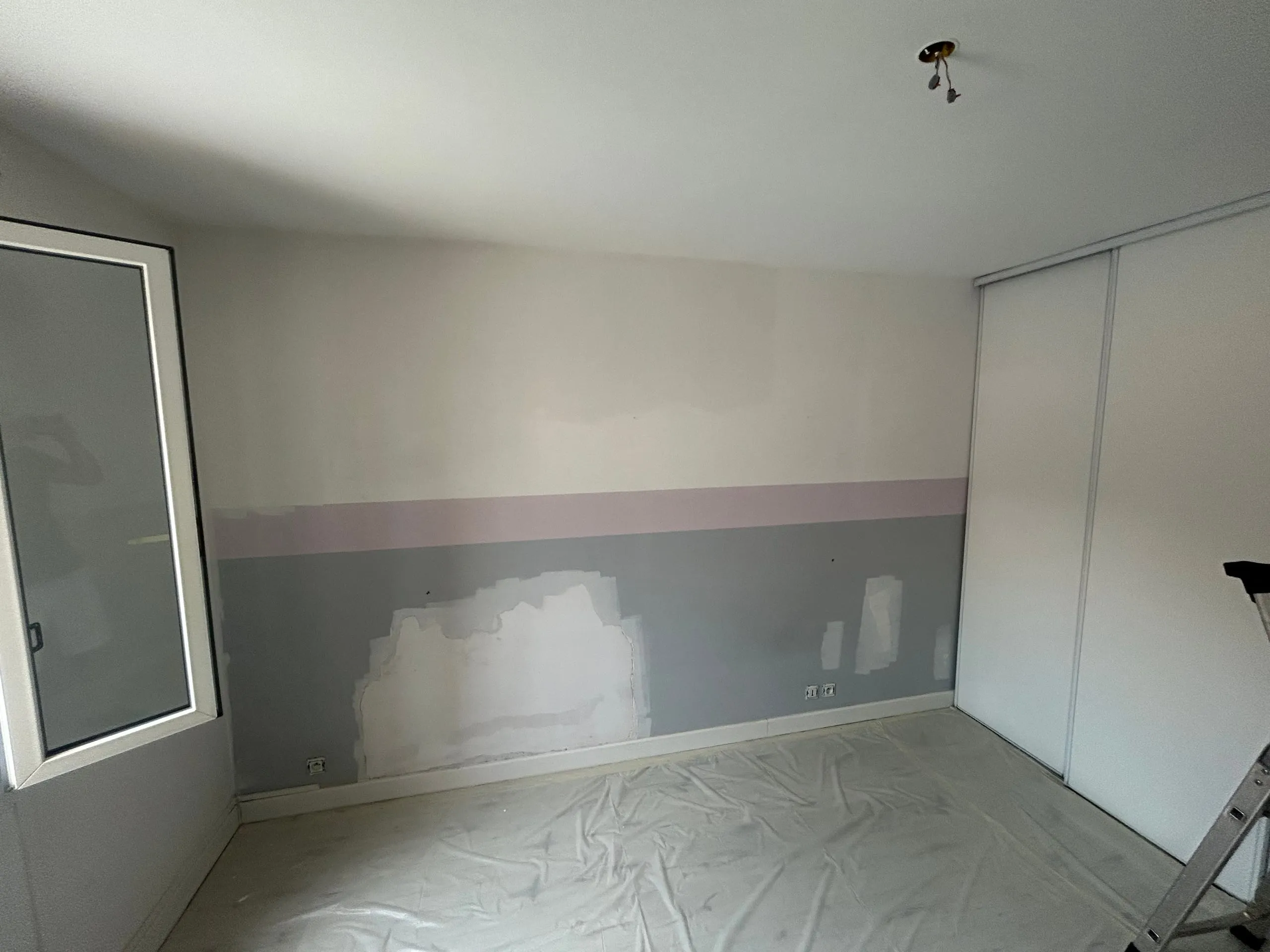 Pièce intérieure en cours de rénovation avec murs partiellement préparés, sol protégé et escabeau visible.