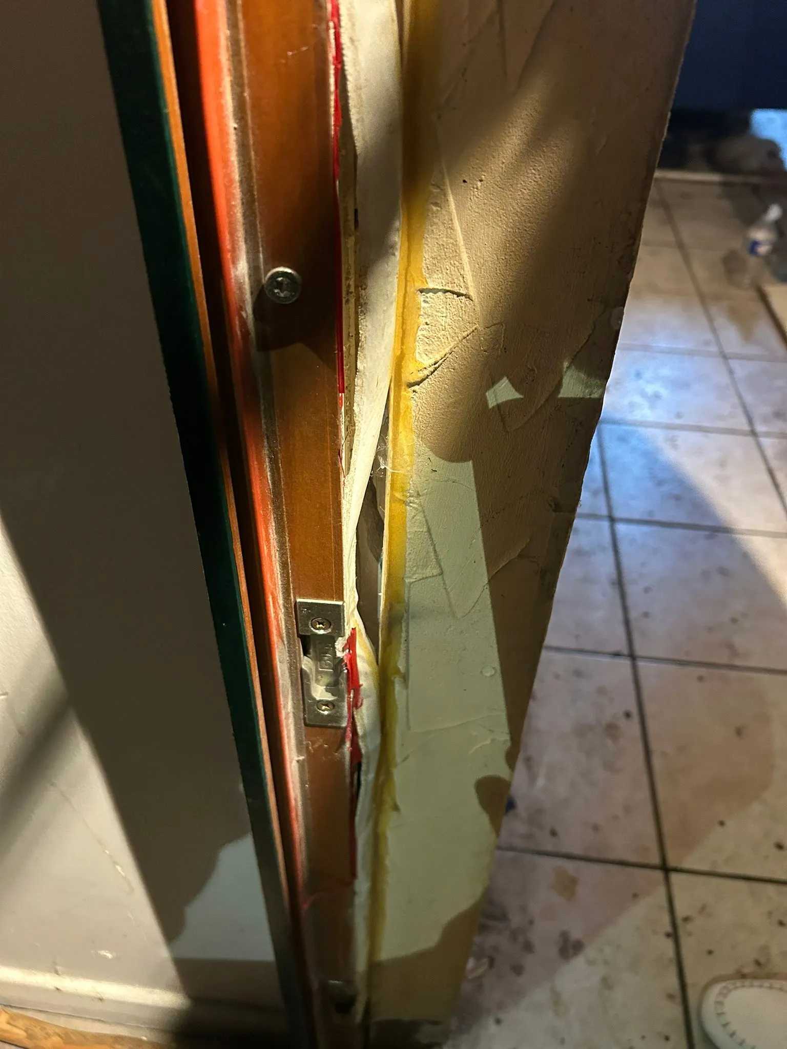 Gâche de porte fixée sur un montant en bois près d’un mur clair.
