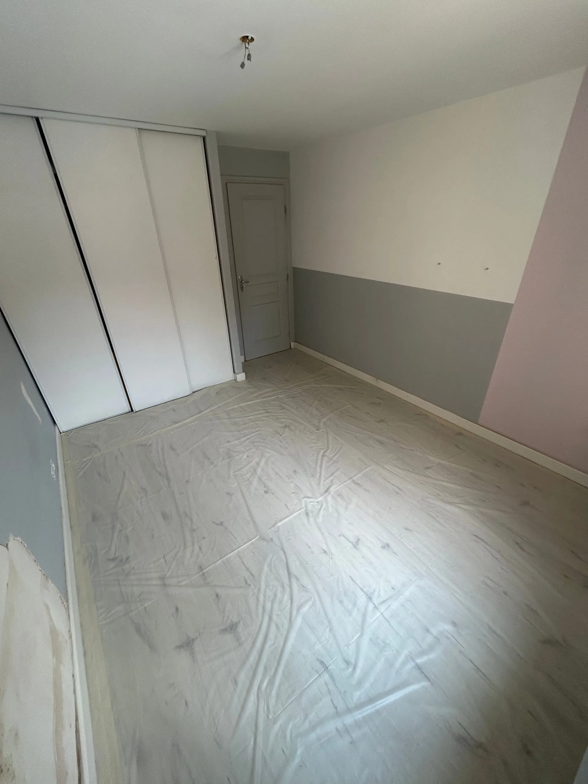 Chambre en cours de préparation avec murs gris, blanc et rose et sol protégé.