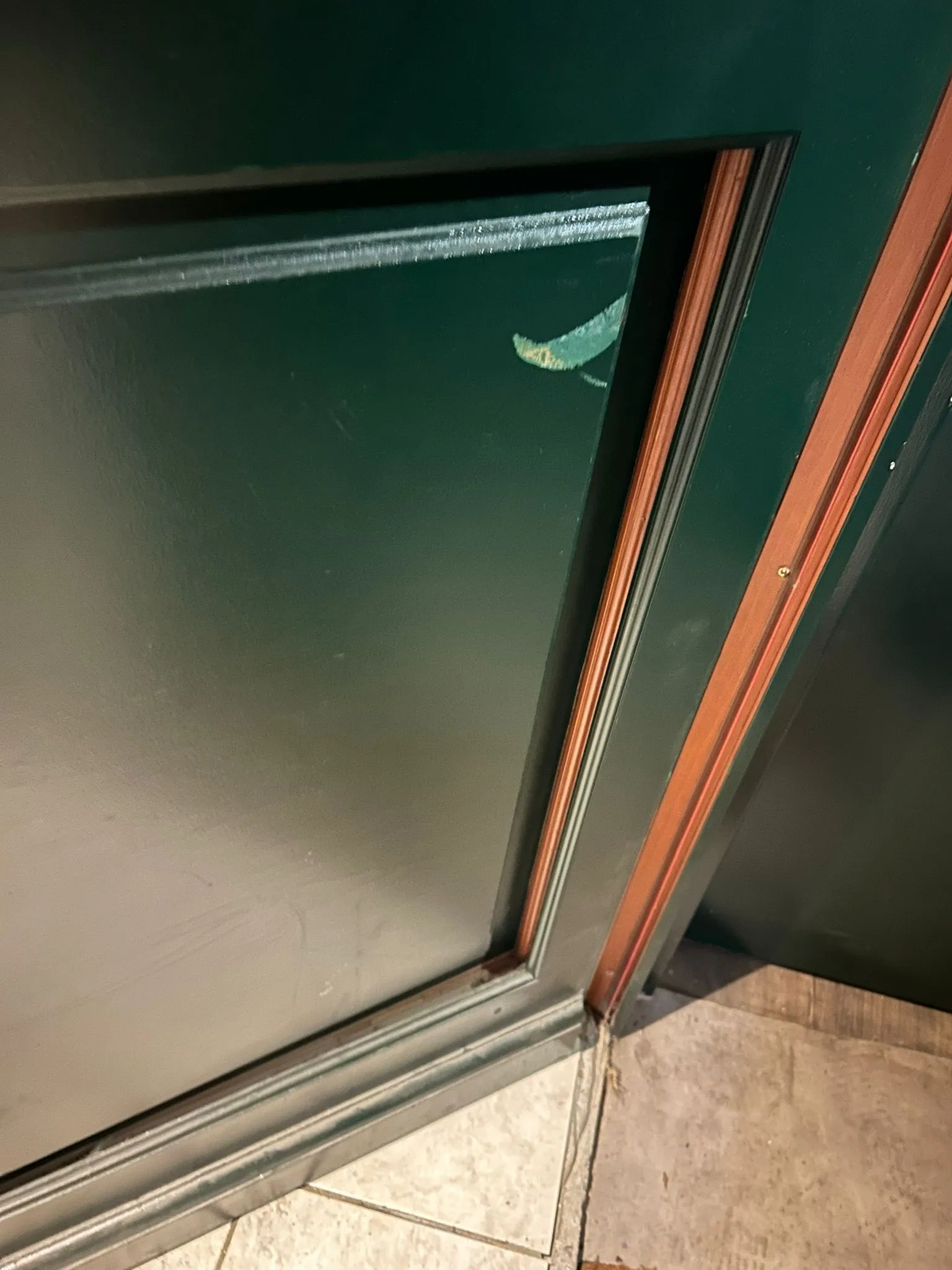Panneau d’une porte peinte en vert avec ses parcloses en bois, vu en contre-plongée près du seuil.