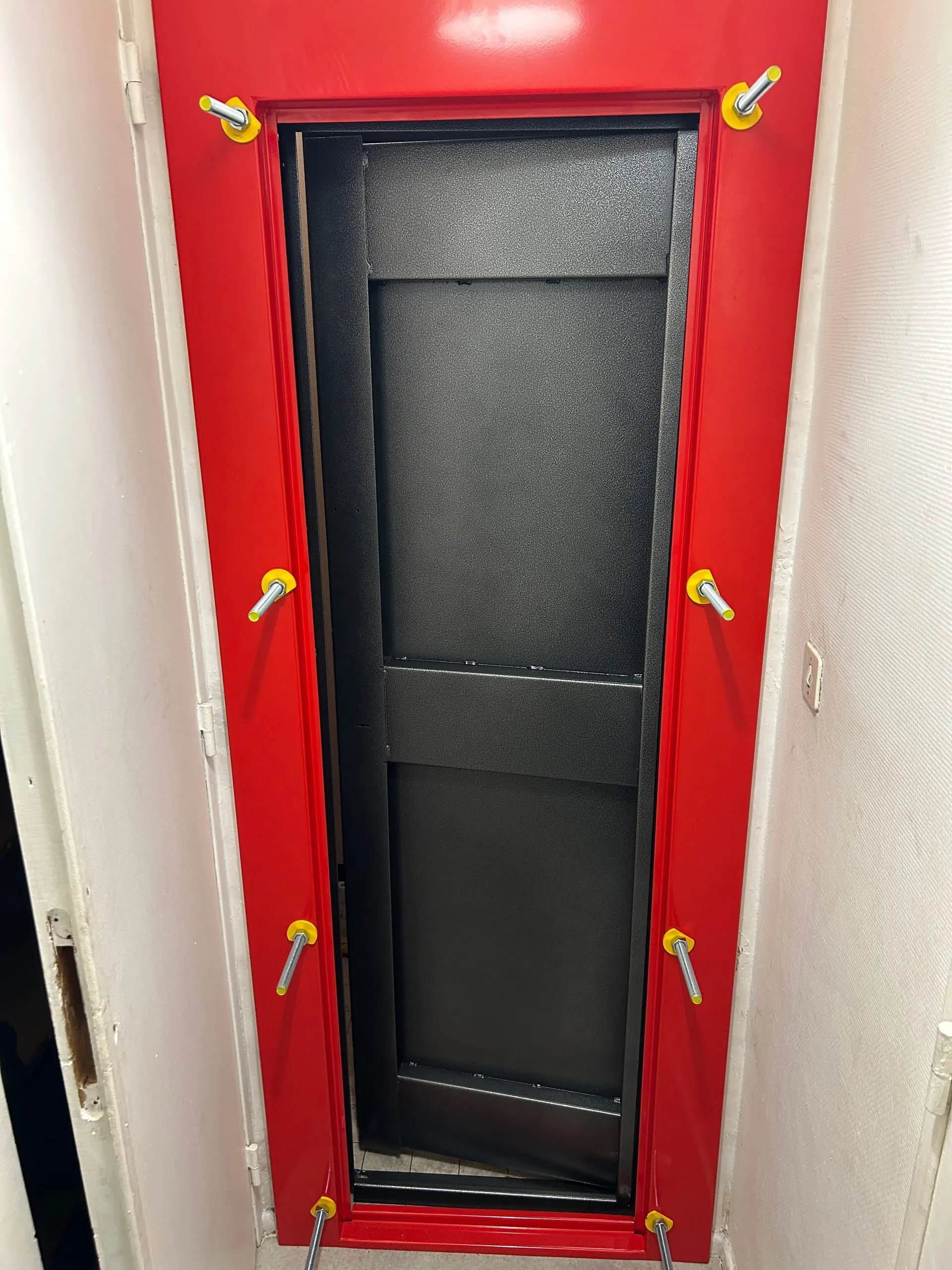 Porte anti-squat en acier anthracite posée dans un encadrement rouge, vue de l’intérieur du local.