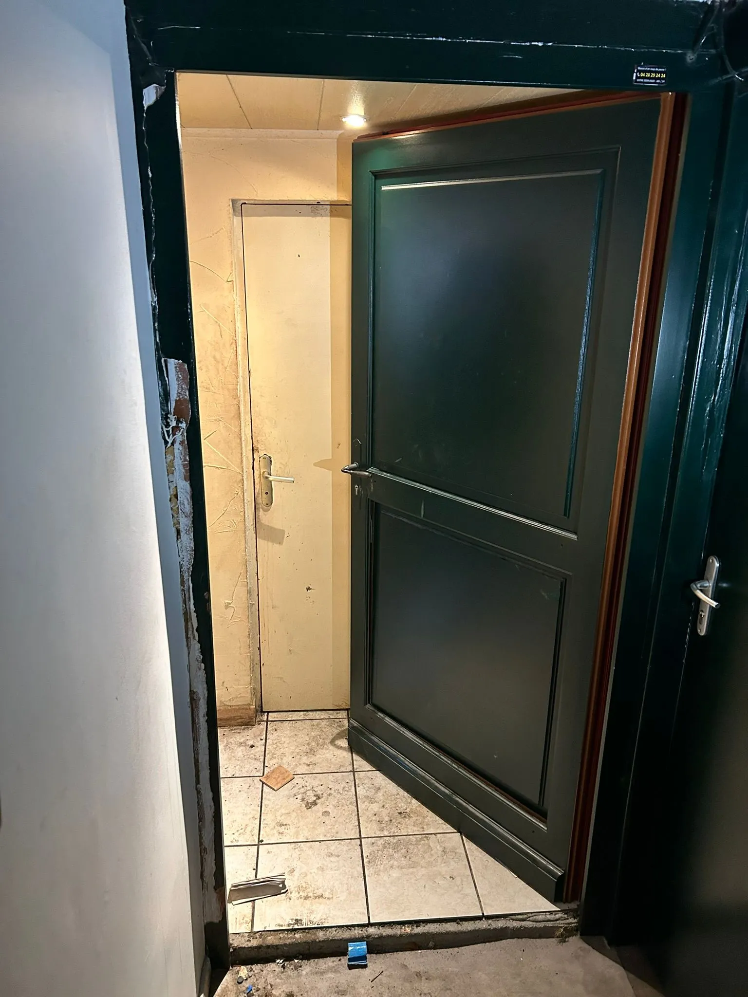 Porte en bois peinte en vert ouverte devant un cadre endommagé après une effraction.