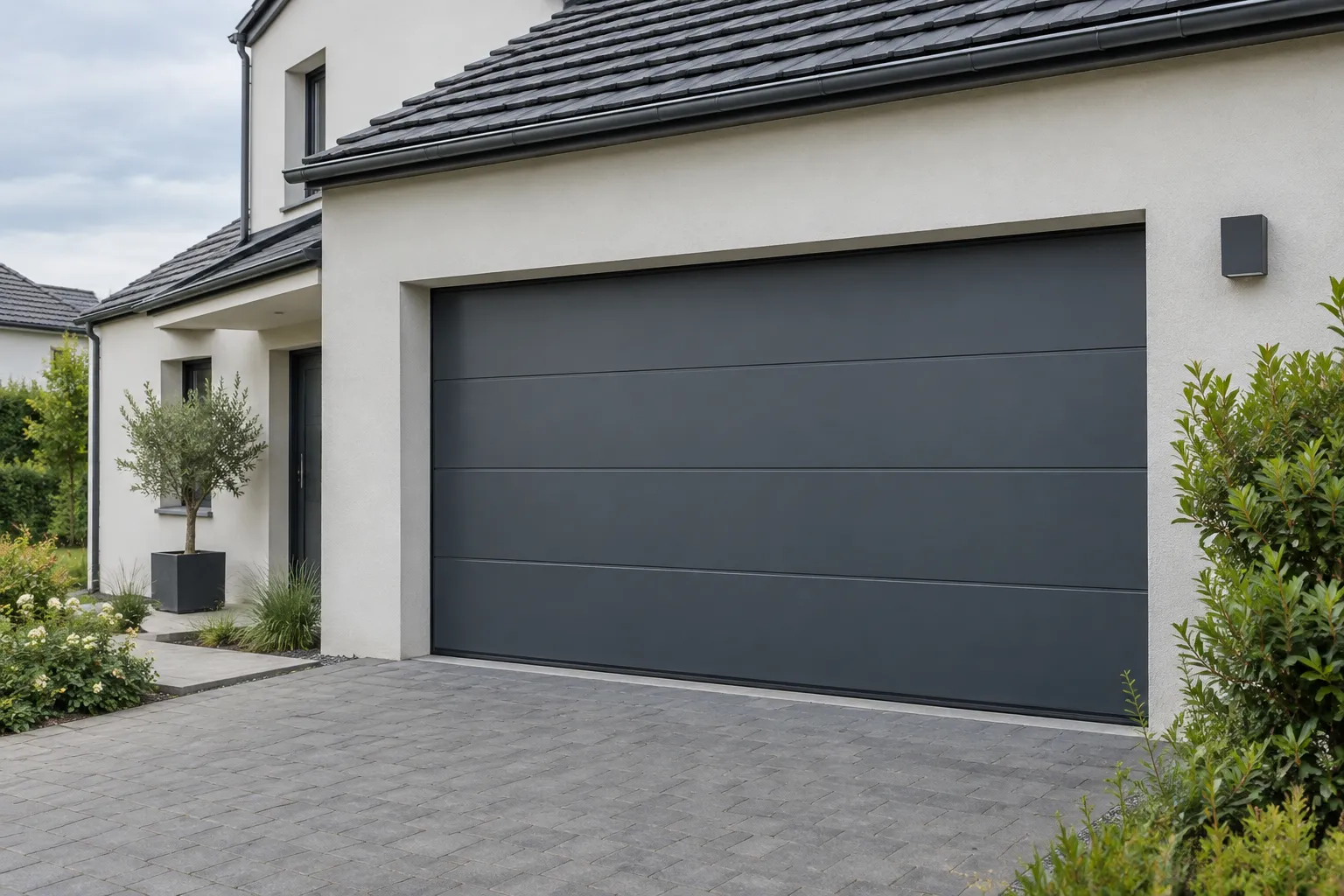 Porte de garage sectionnelle anthracite fermée sur la façade claire d’une maison.