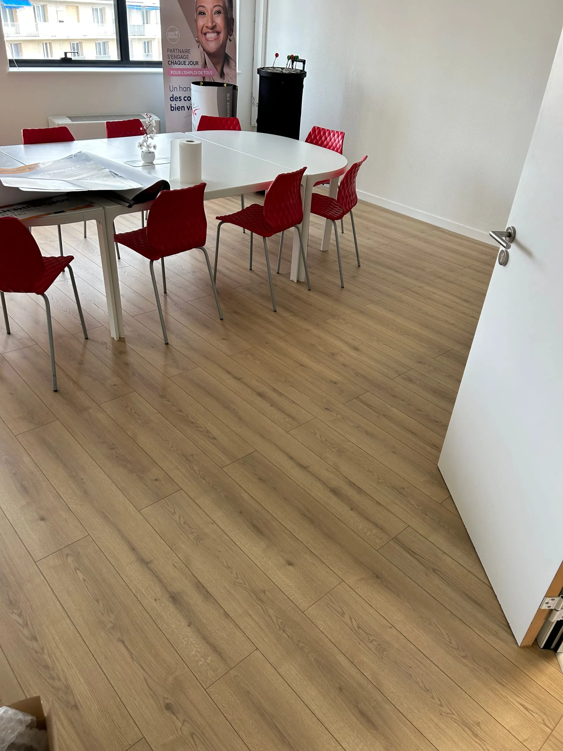 Salle de réunion avec table blanche, chaises rouges et parquet flottant bois.