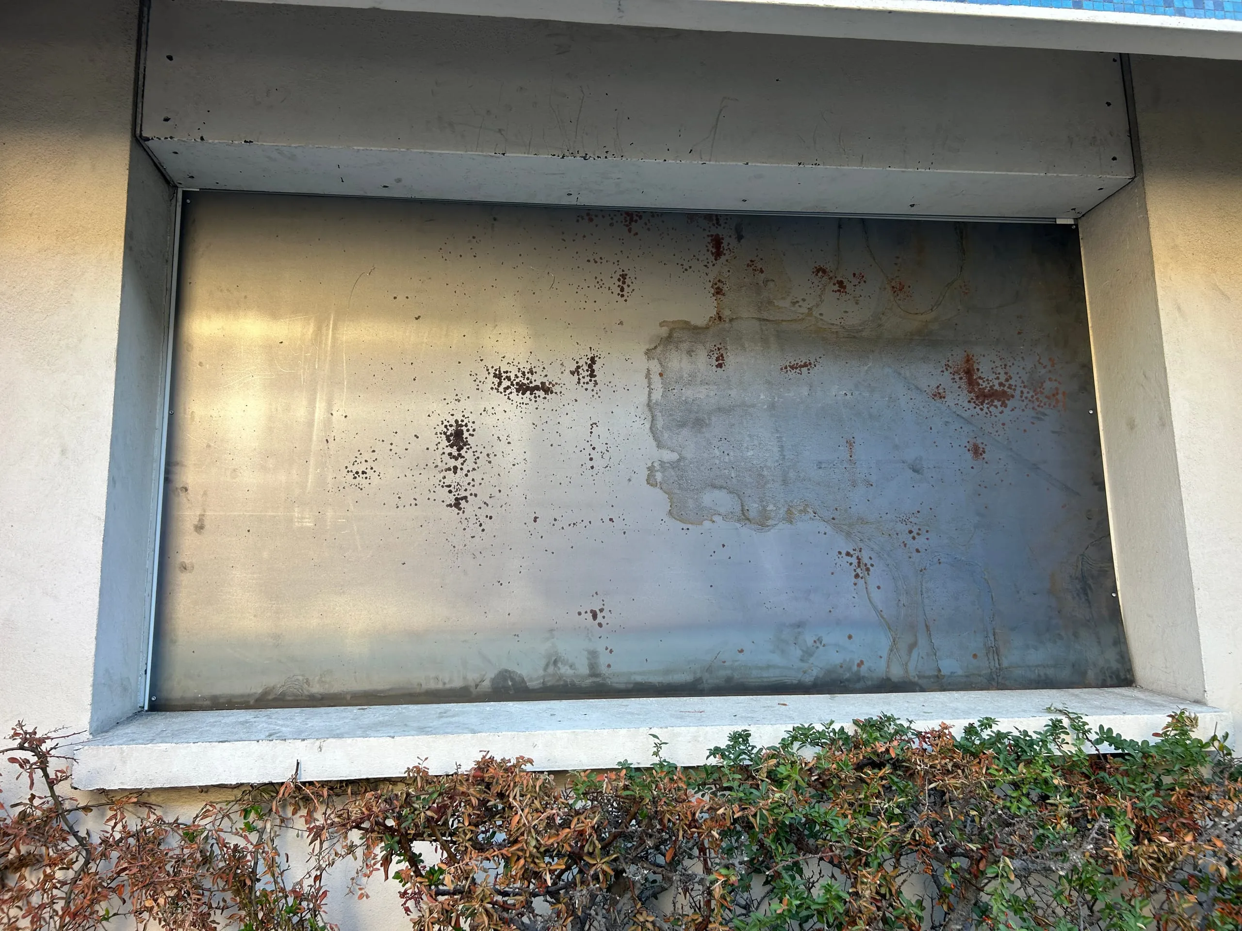 Grande tôle d’acier posée dans une ouverture de façade, avec des traces de rouille.