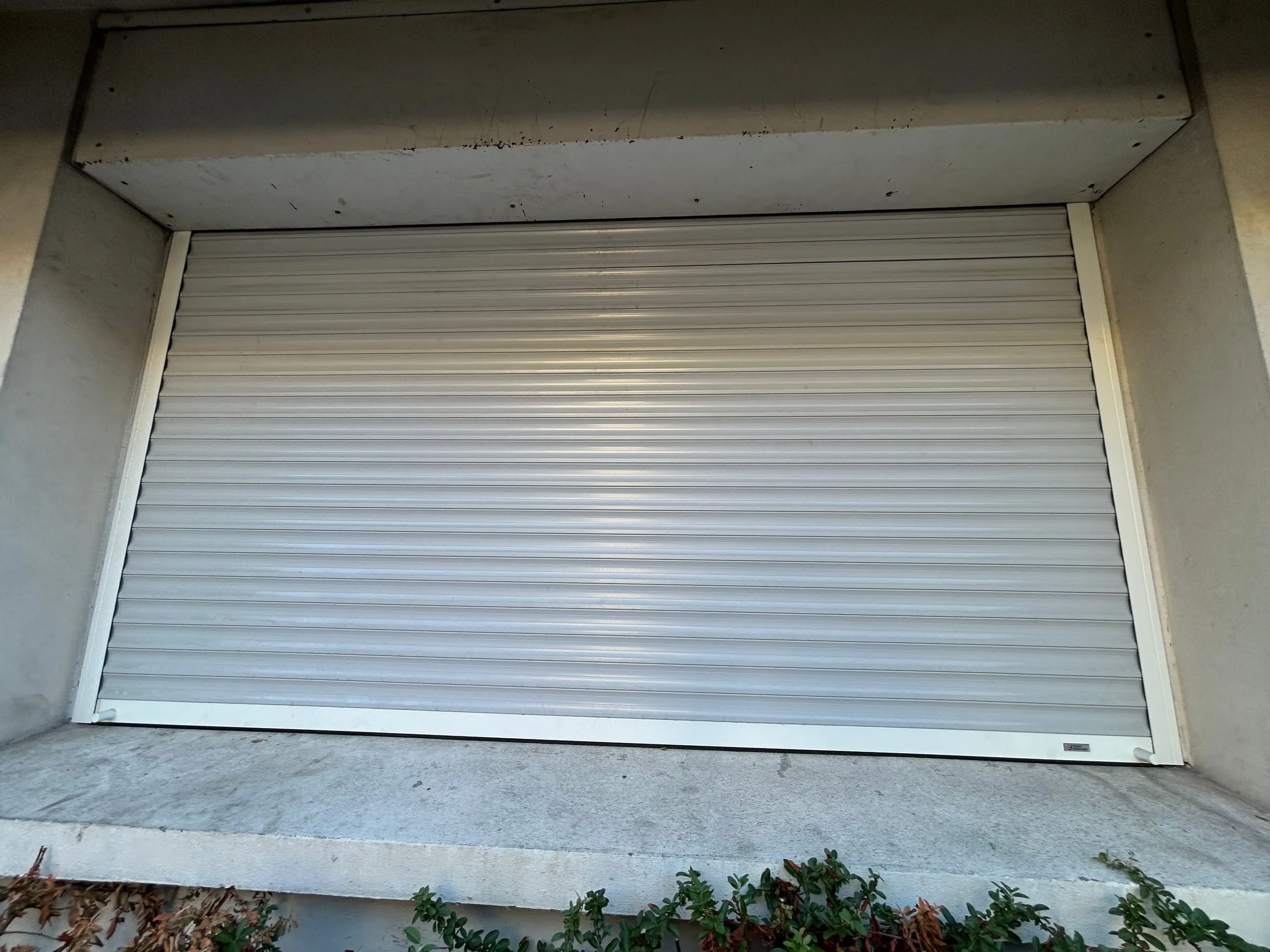 Volet roulant aluminium blanc fermé dans l’embrasure d’une façade claire.